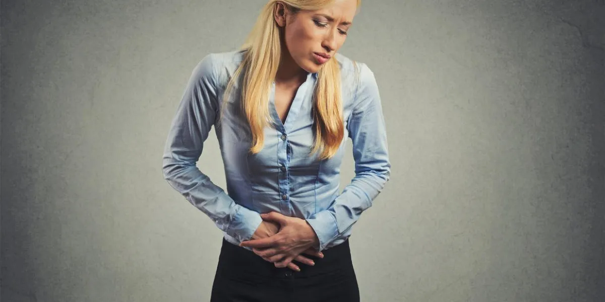 woman suffering from severe pain in her tummy isolated on gray wall background