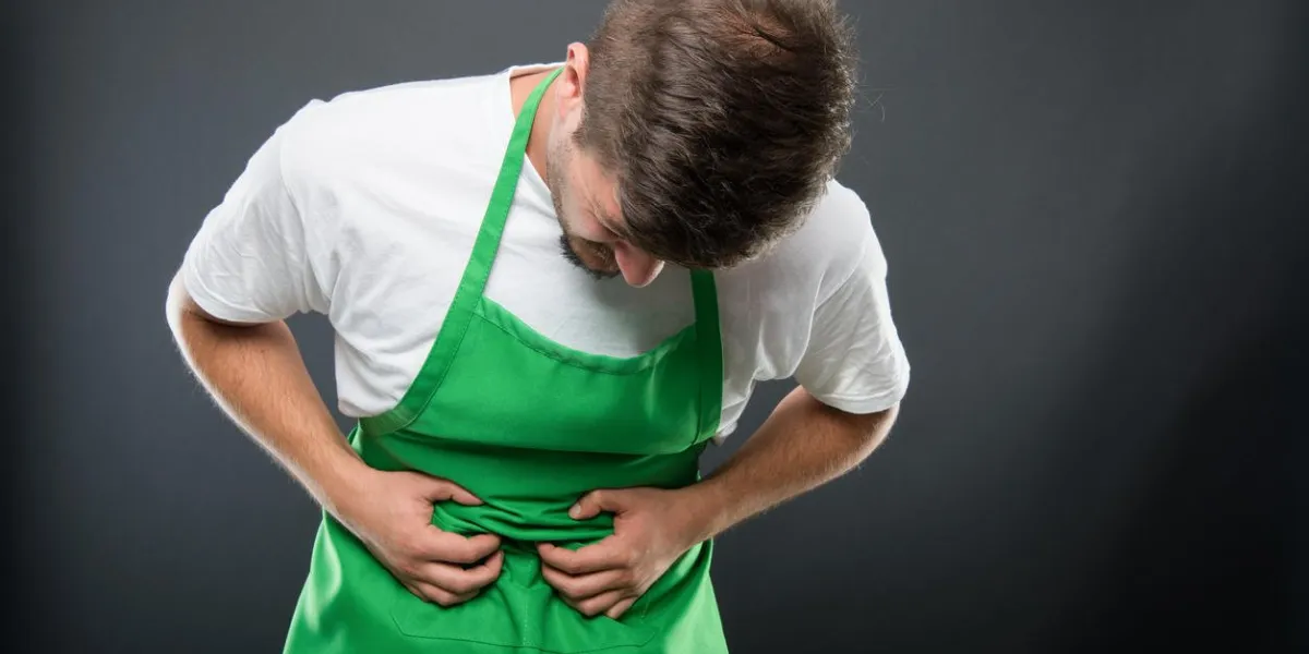 portrait de l'employeur de supermarché tenant le ventre comme blesser sur fond noir