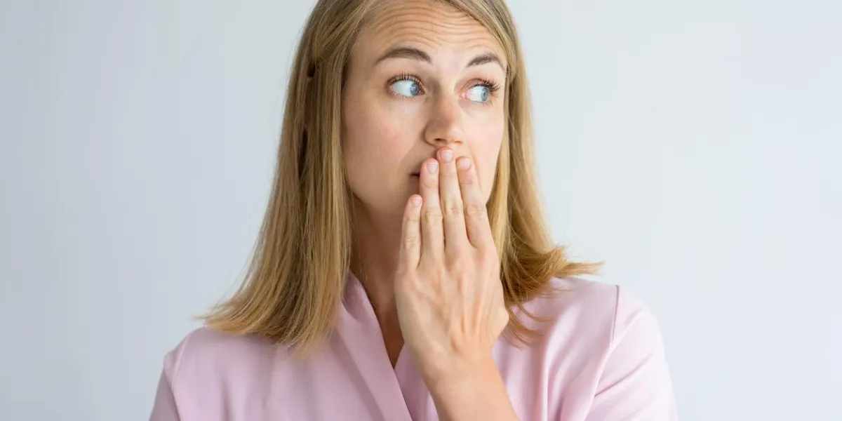 portrait of shocked young caucasian woman wearing pink blouse covering mouth with hand fear, bad breath concept