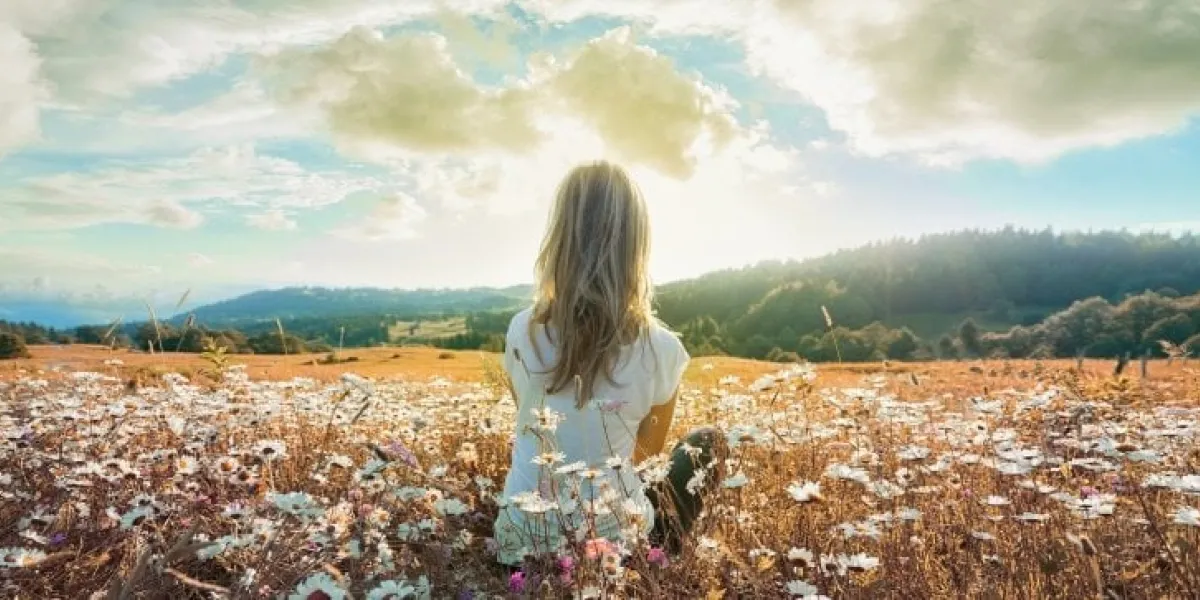 woman sitting on the chamomiles field and looking at the cloudy sky at sunset banner edition