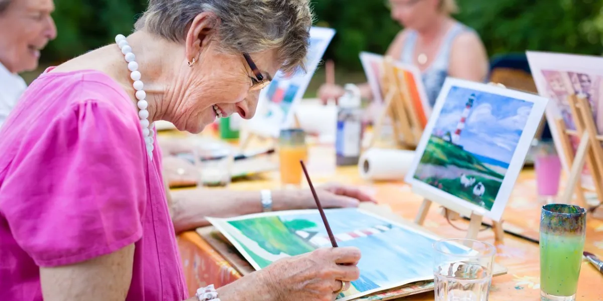 side view of a happy senior woman smiling while drawing as a recreational activity or therapy outdoors together with the group of retired women