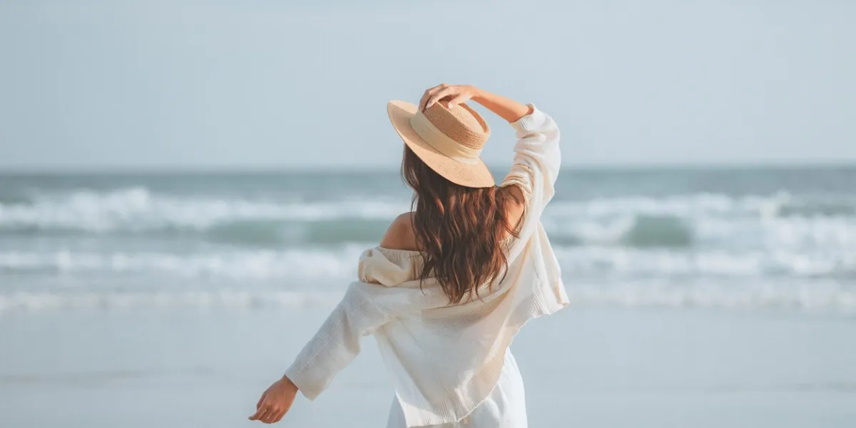 summer beach vacation concept, young woman with hat relaxing with her arms raised to her head enjoying looking view of beach ocean on hot summer day, copy space