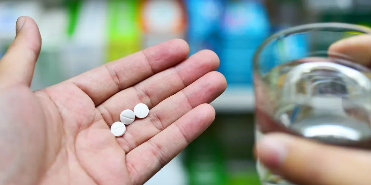 man's hand hold medicine tablets and bottle, pharmacy medicines shelves in the background