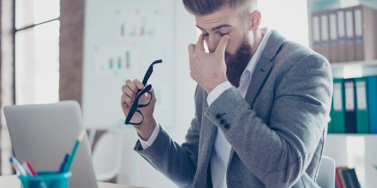 tired and overworked stylish red bearded manager sitting in front of computer and trying to concentrate, his eyes are dry and hurt