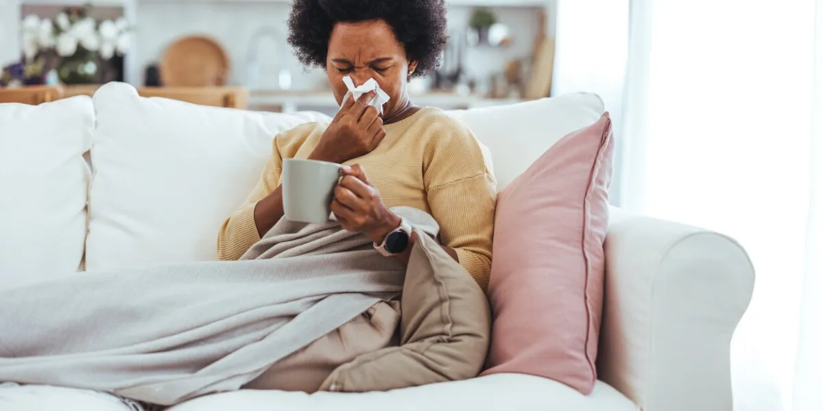 shot of a mature woman blowing her nose with a tissue at home woman sneezing in a tissue in the living room worried african american woman sitting at home while being sick