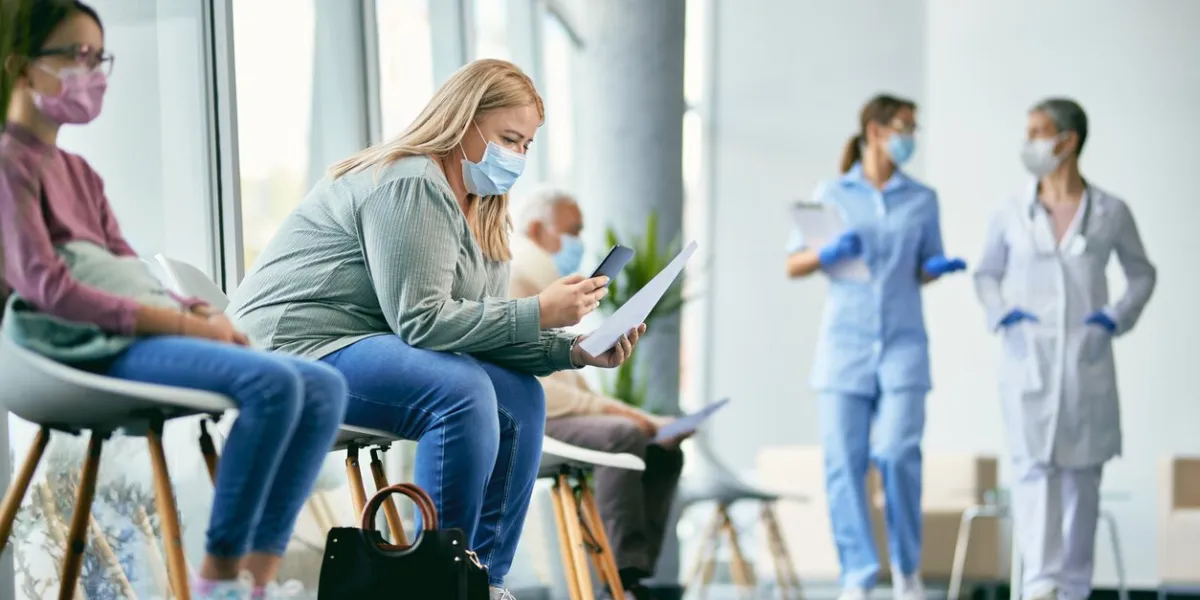 female patient examining medical paperwork and using mobile phone while sitting in hallway at the hospital