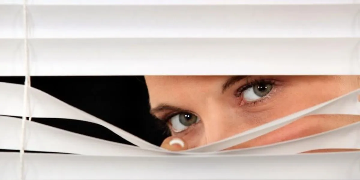woman peeking through venetian blinds
