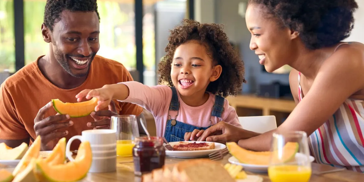 family shot with parents and daughter at home having breakfast spreading jam on bread at table