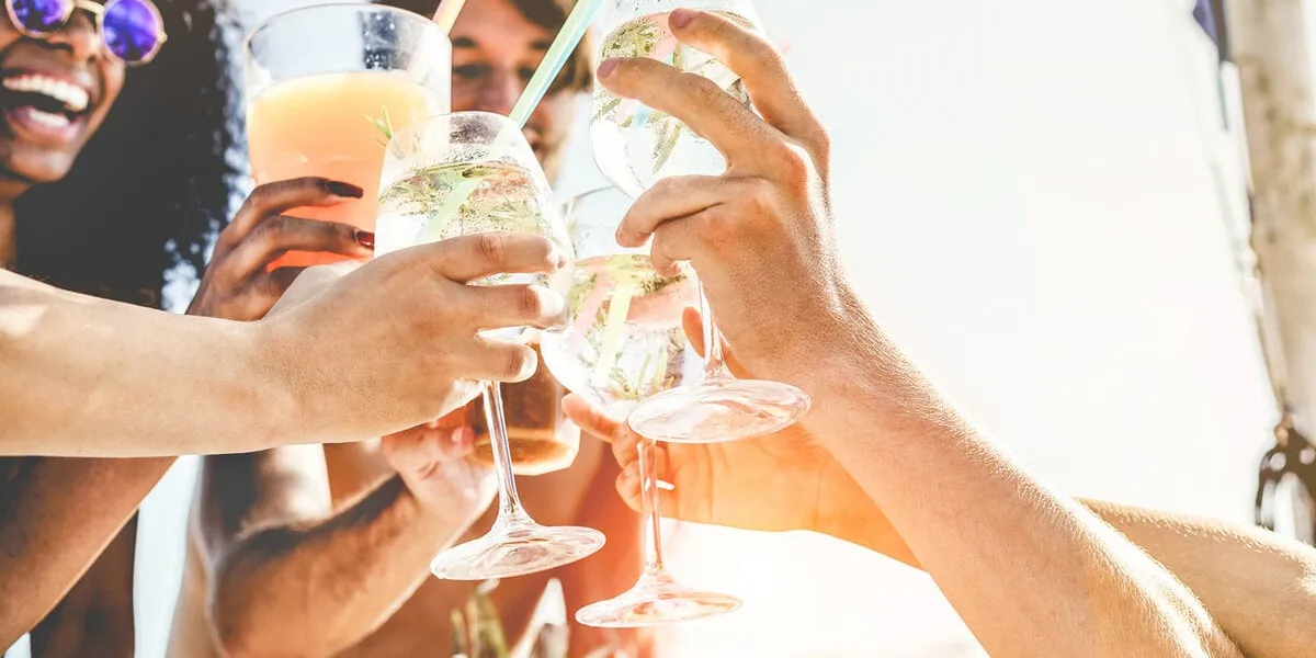 group of happy friends cheering with tropical cocktails at boat party - young people having fun in caribbean sea tour - youth and summer vacation concept - focus on bottom hands glass