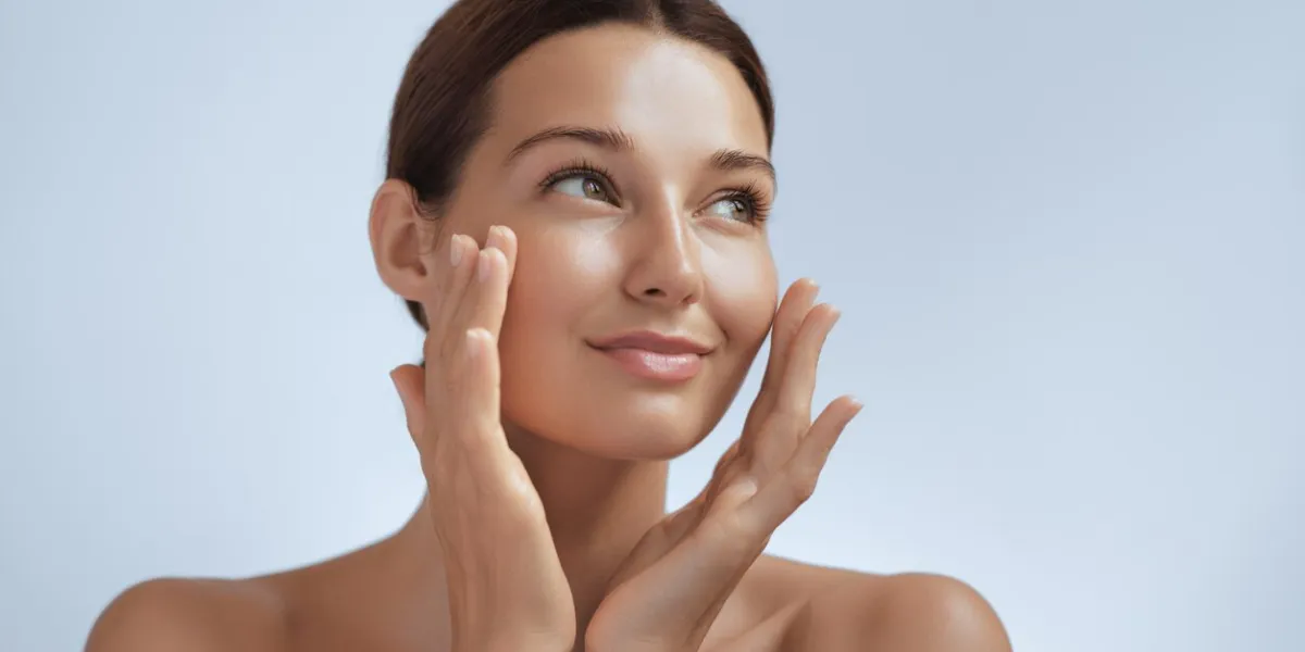 skincare woman with beautiful face touching healthy facial skin beautiful portrait of smiling asian girl model with natural makeup enjoys glowing hydrated skin on blue background closeup high-quality photo