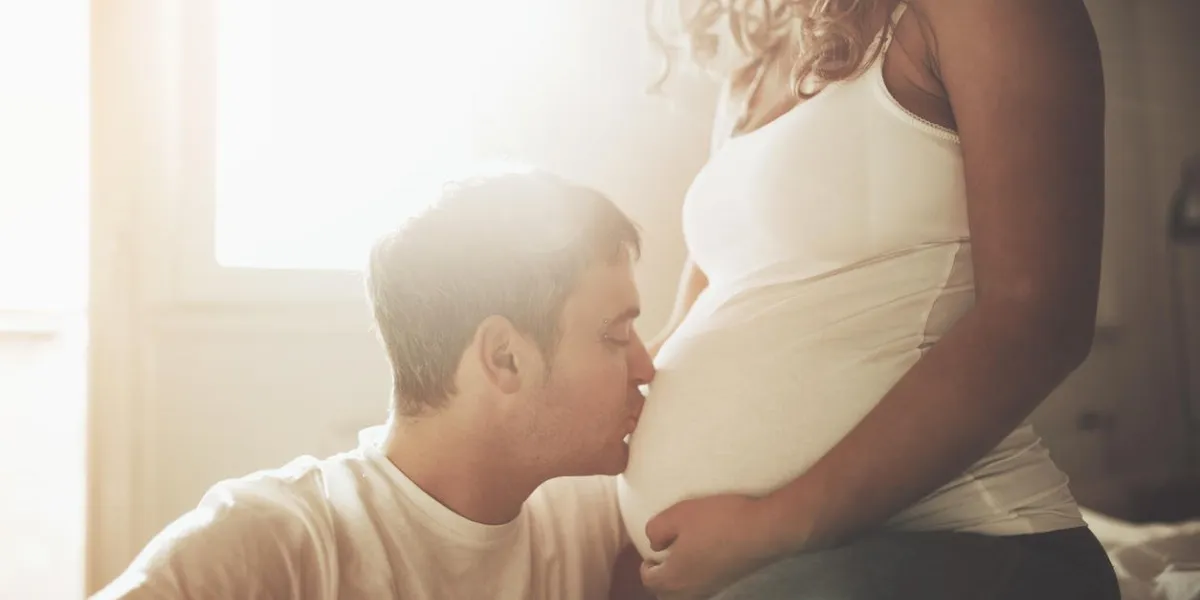 husband kissing newborn through wife belly