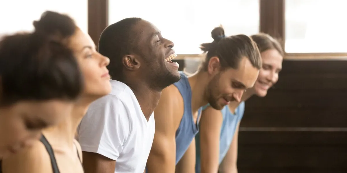 african man beginner laughing having fun trying to do yoga pose, push ups plank or stretching in upward facing dog exercise at group training class with multiracial diverse people, closeup side view