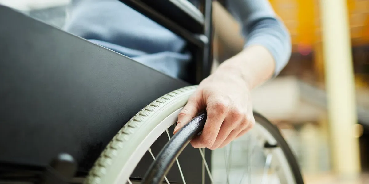 close-up of young female patient sitting in wheelchair and holding the wheel while going at hospital