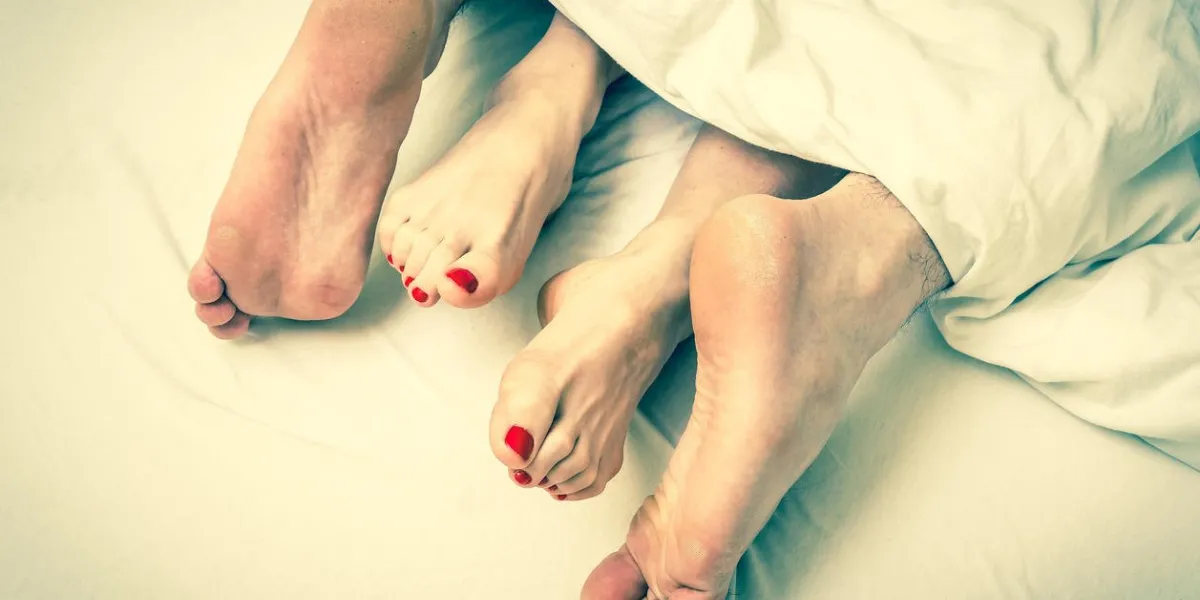 close-up of four feet in a bed under the white blanket