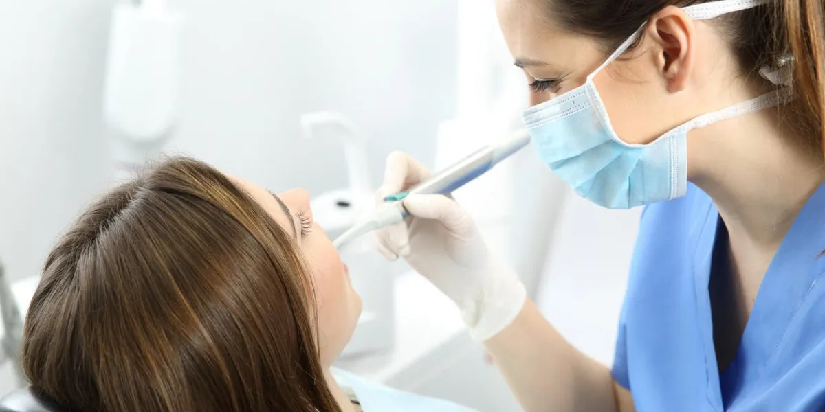 close up of a dentist working with a patient teeth sitting on a chair in a clinic box with medical equipment in the background