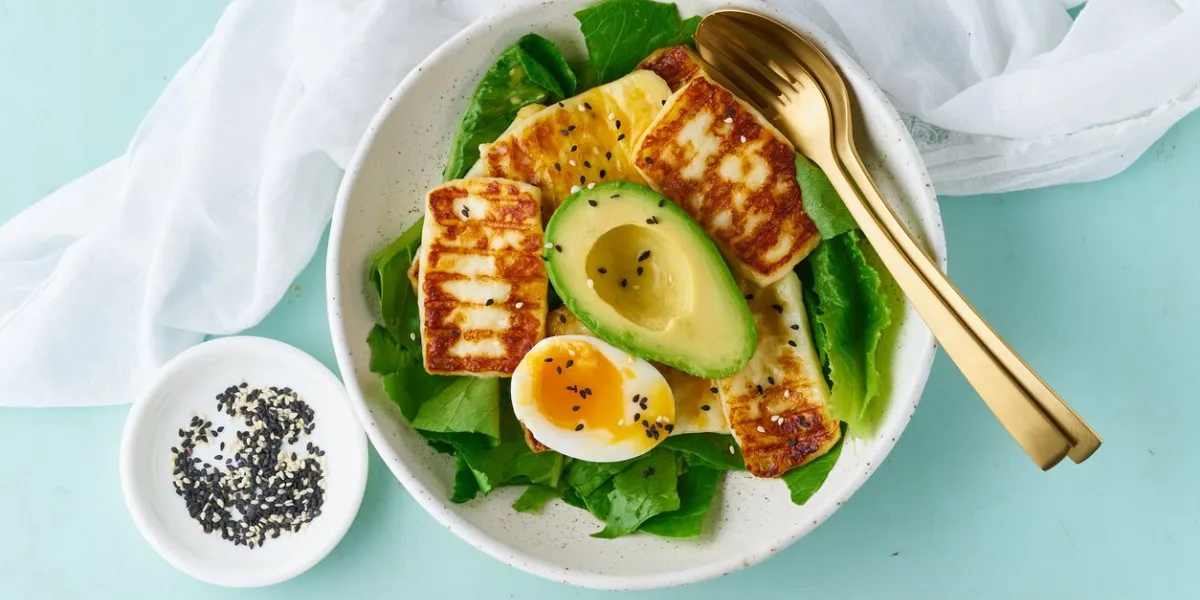 keto ketogenic diet soft boiled eggs with grilled haloumi, avocado and lettuce, mediterranean cuisine on pastel background
