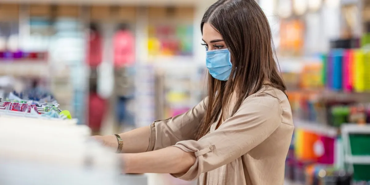 woman wearing face mask push shopping cart in supermarket department store girl choosing, looking grocery things to buy at shelf during coronavirus crisis or covid19 outbreak