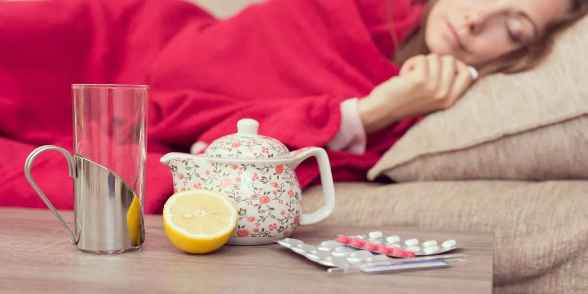 femme malade recouverte d'une couverture couchée dans son lit avec une forte fièvre et une grippe, théière au repos, des pilules et du citron sur la table, se concentrer sur le citron et une théière
