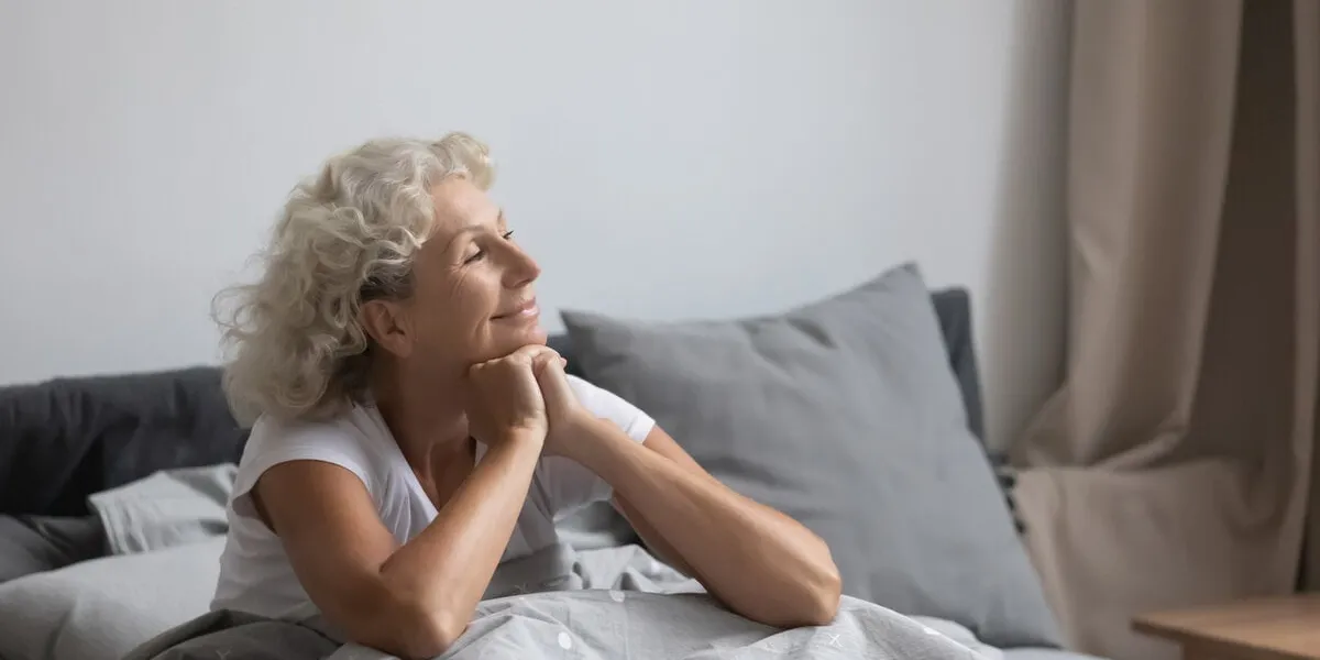 peaceful calm positive middle aged senior retired woman sitting in bed after wakeup in weekend morning, enjoying good mood after good night rest relaxation, welcoming new day alone in bedroom