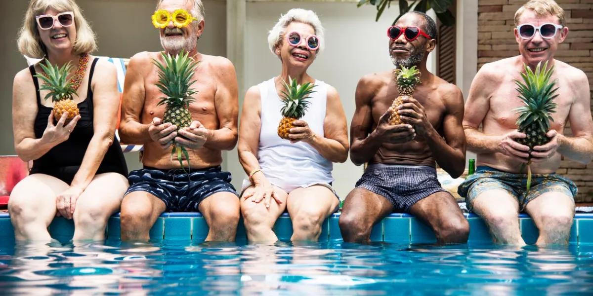 group of diverse senior adults sitting at poolside holding pineapples together