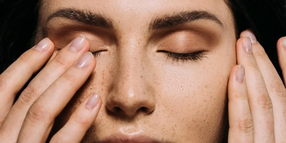 close up view of tender girl with freckles on face touching closed eyes
