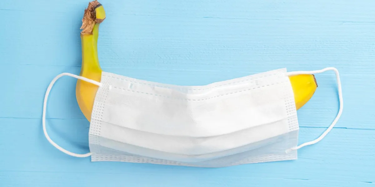 yellow ripe banana covered with a white medical protective mask on a wooden light blue background close-up the concept of protected sex and contraception strengthening immunity for the treatment of coronavirus