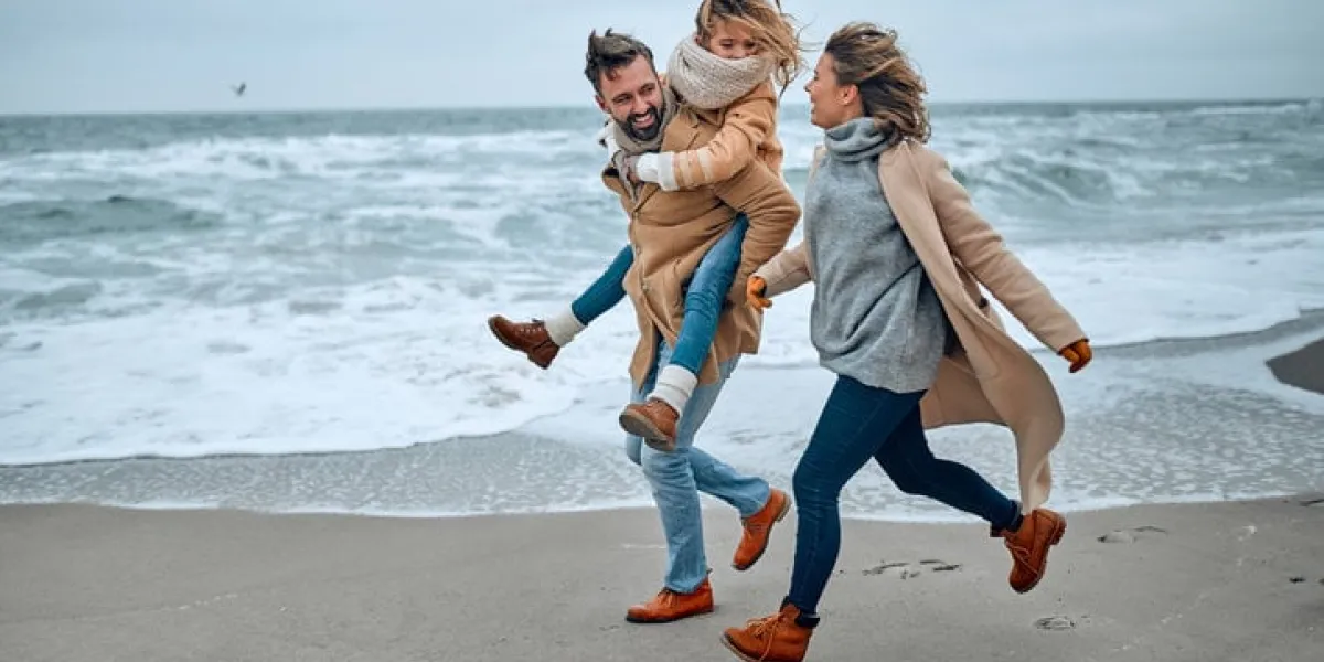 portrait of a young married couple and their cute daughter who have fun on the beach in winter