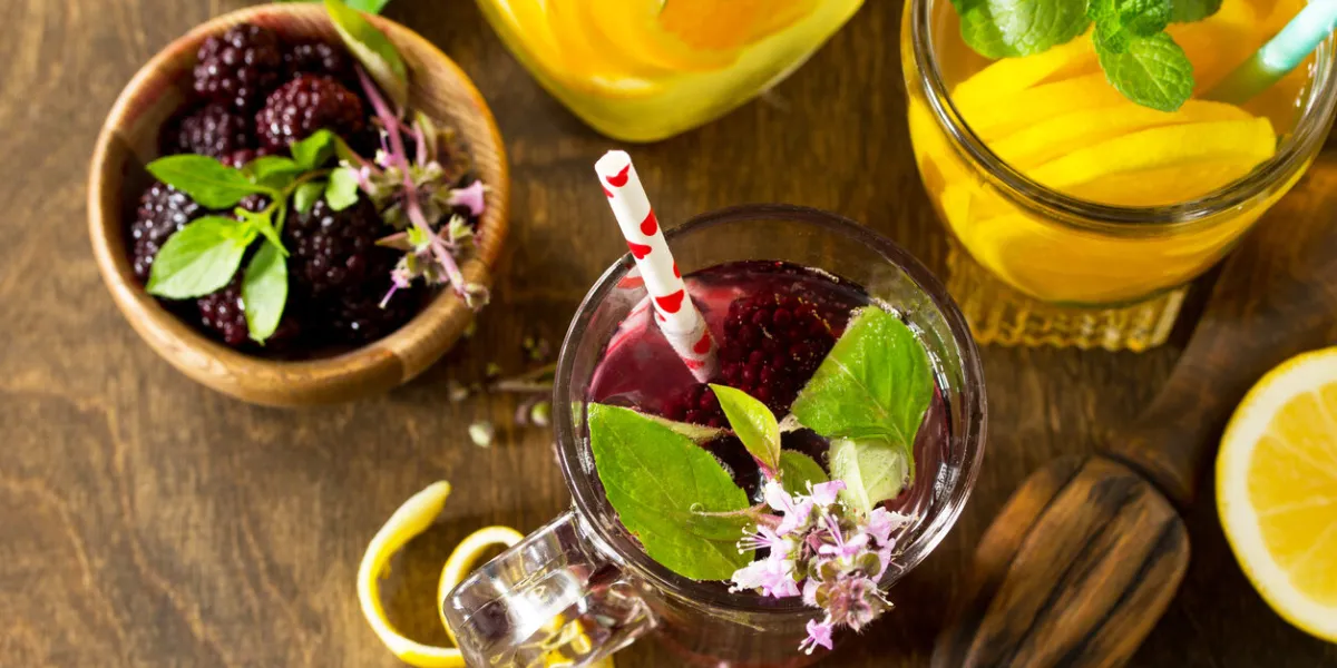 refreshing summer berry lemonade, lemon mint tea and orange lemonade with rosemary on wooden table in rustic style