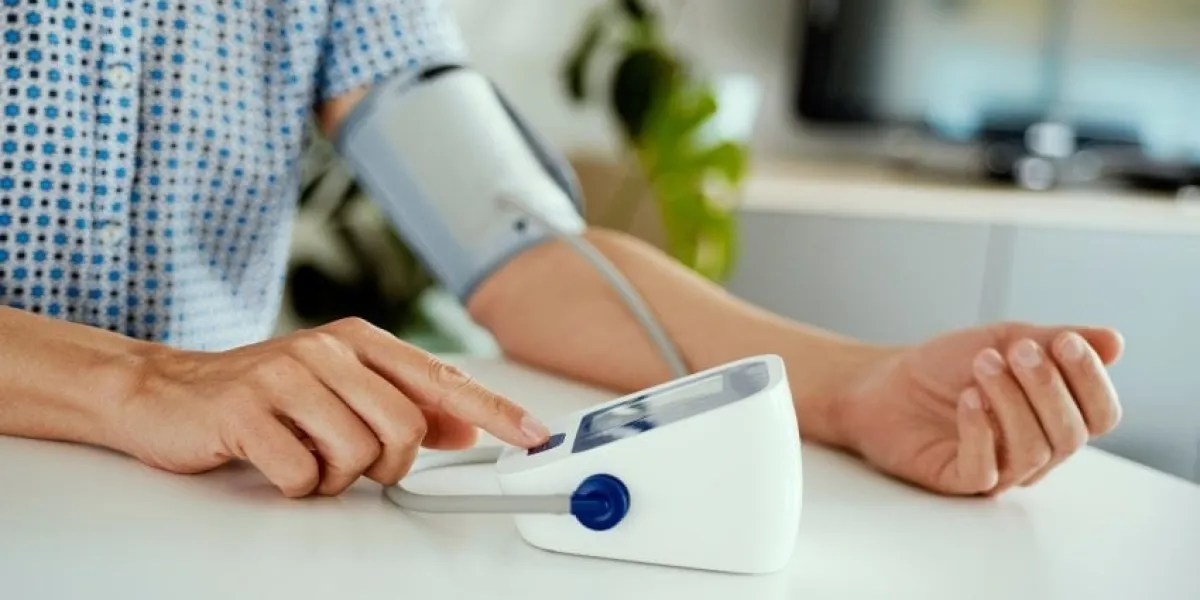 closeup of a caucasian man measurins his blood pressure with an electronic sphygmomanometer, sitting at a white table