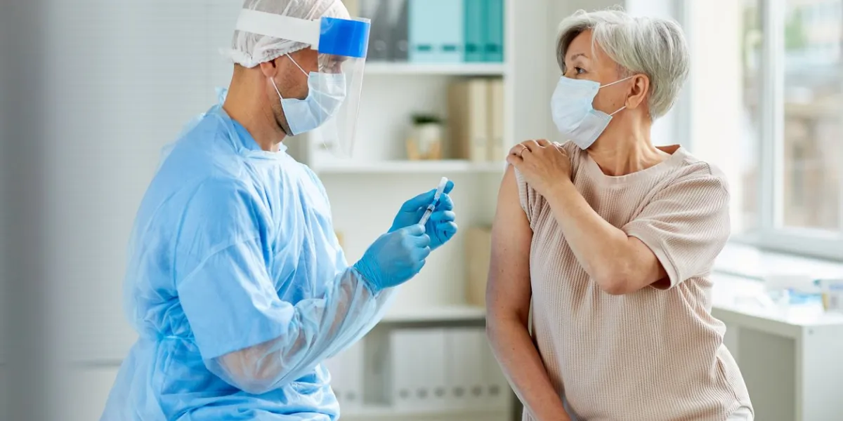 side view shot of male nurse wearing protective mask and gloves preparing medical syringe for giving injection to senior patient