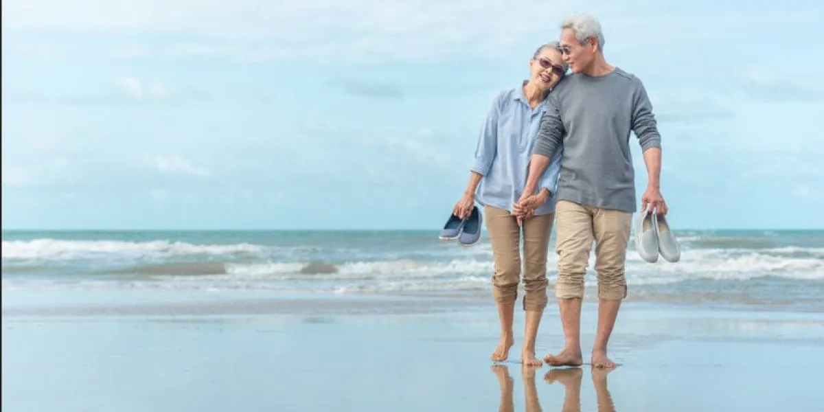 age, travel, tourism and people concept - happy senior couple holding hands and walking on summer beach