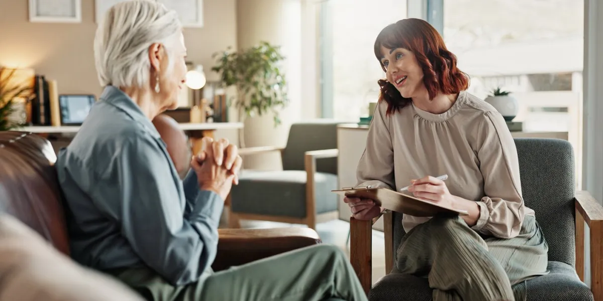 senior woman, psychologist and clipboard for counselling, help and smile for support in office therapist, document and checklist for advice, listen or empathy for retirement mental health meeting