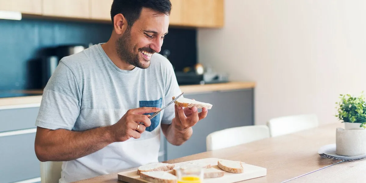 man spreading cream cheese on baguette slice on wood board