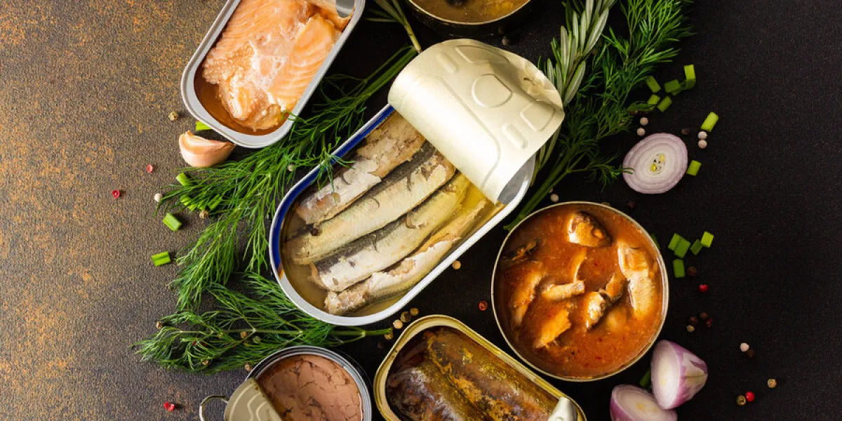different open tin cans with canned fish among spices and herbs on a brown background, canned salmon and mackerel, sprat and sardine, tuna and herring and fish pate, top view