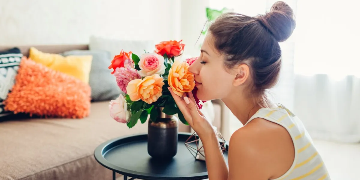 woman smelling fresh roses in vase on table housewife taking care of coziness in apartment interior design and decor with flowers