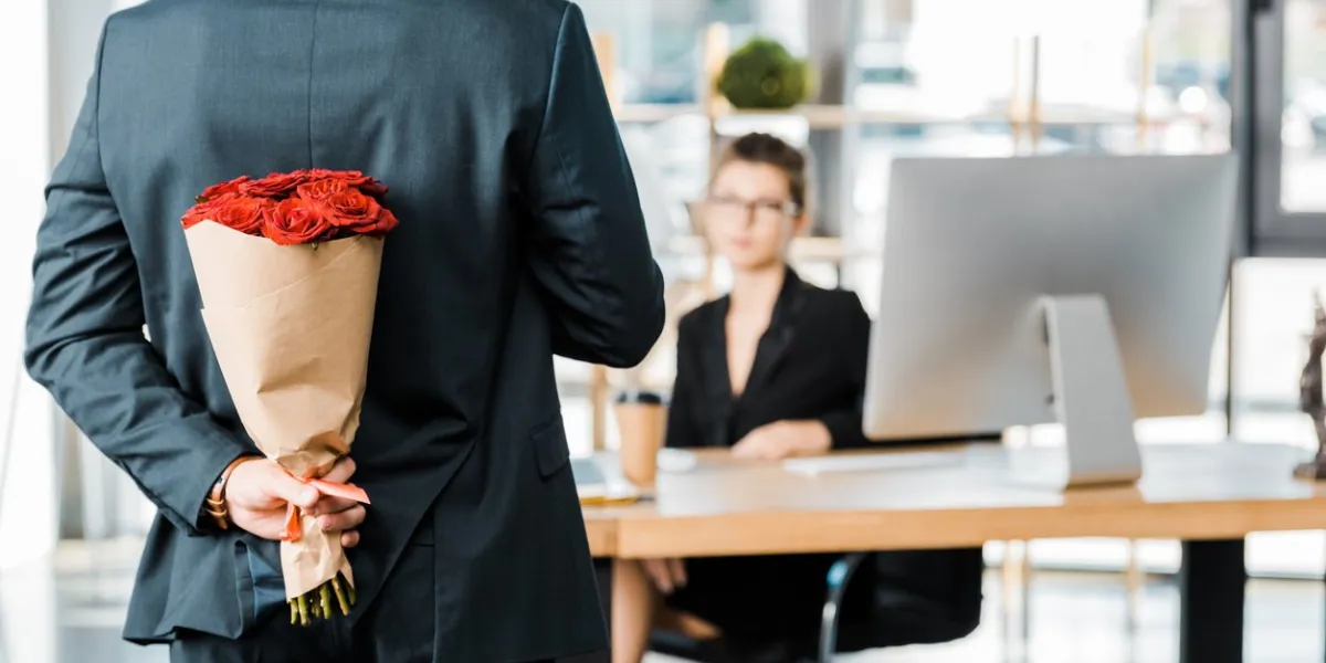 cropped image of businessman hiding bouquet of roses behind back to surprise businesswoman in office