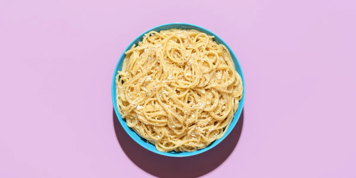 above view with a portion of the pasta cacio e pepe, minimalist on a purple table delicious italian dish, spaghetti with grated cheese and black pepper