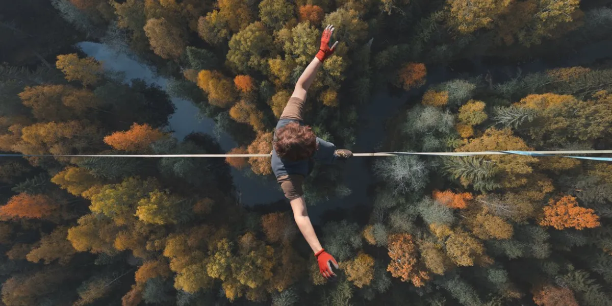 a breathtaking view of a tightrope walker walking along a line high above a beautiful forest topics of highline, longline, extreme activities top view