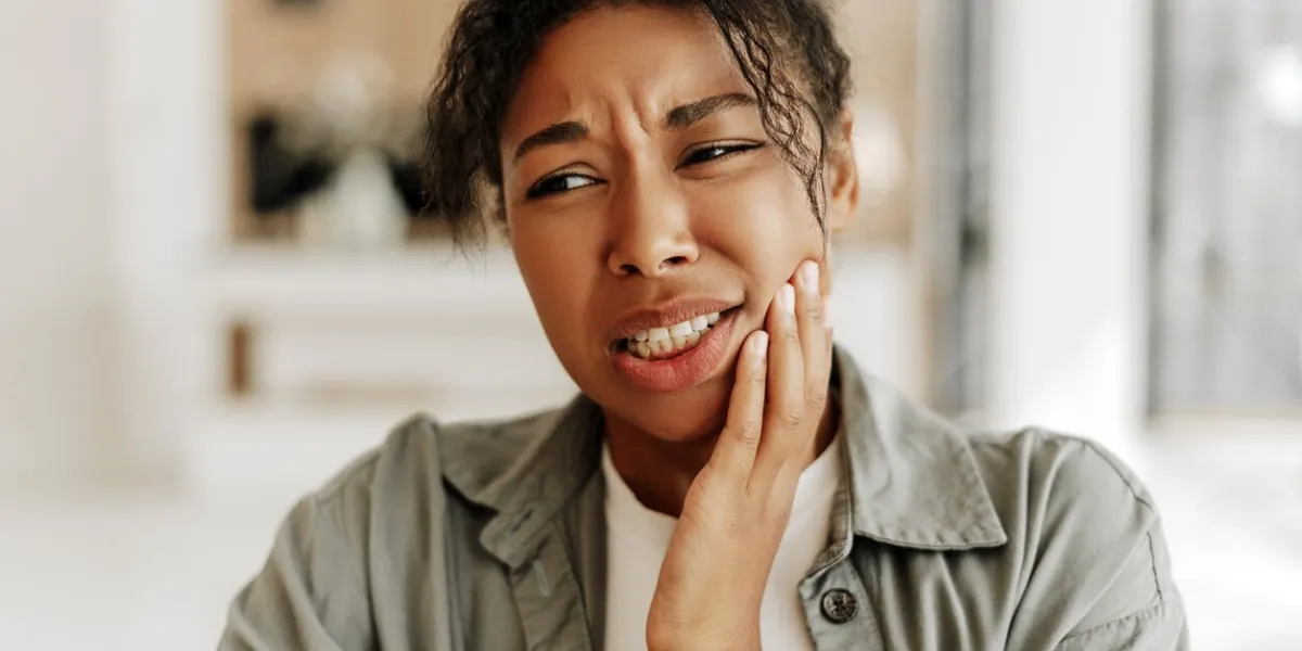 young woman holding her cheek in pain due to a toothache, emphasizing the importance of dental care and hygiene