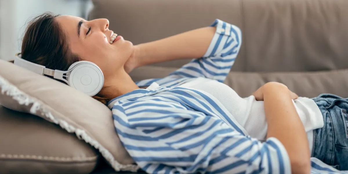 shot of beautiful woman singing while listening music lying on couch in living room at home