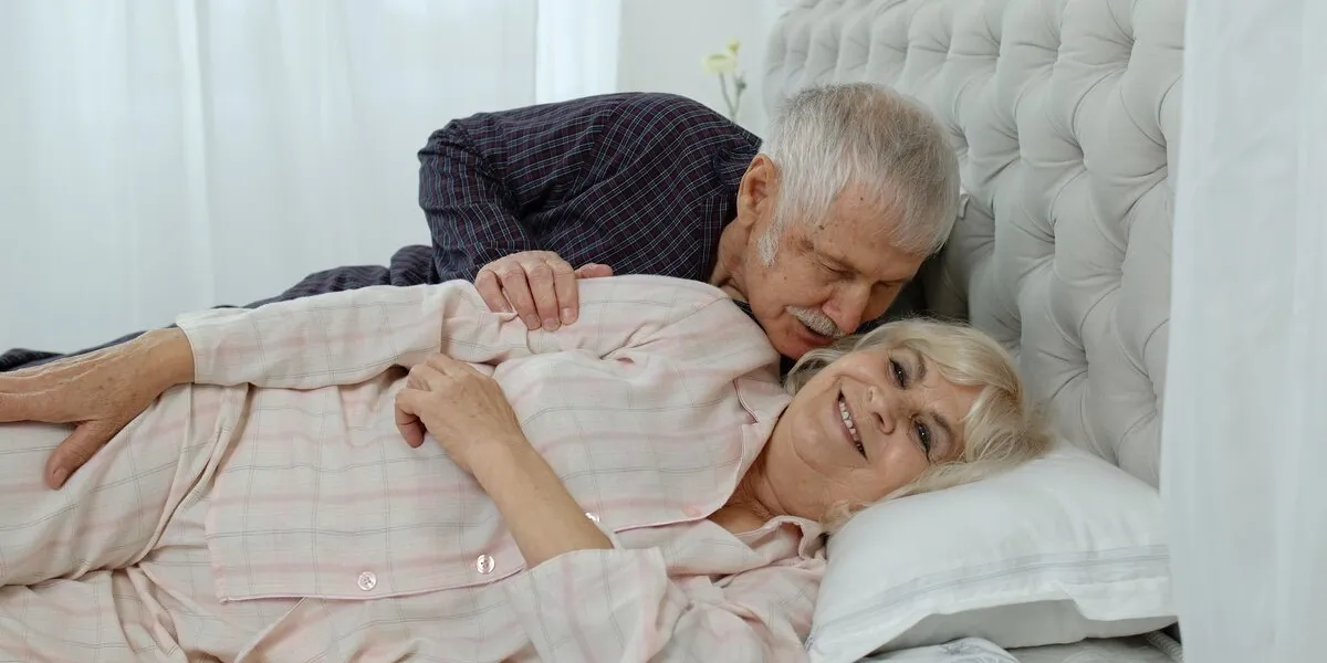 senior caucasian grandparents couple lying in bed at home in morning man gently whispering to woman grandmother and grandfather in love concept of sex in elderly age