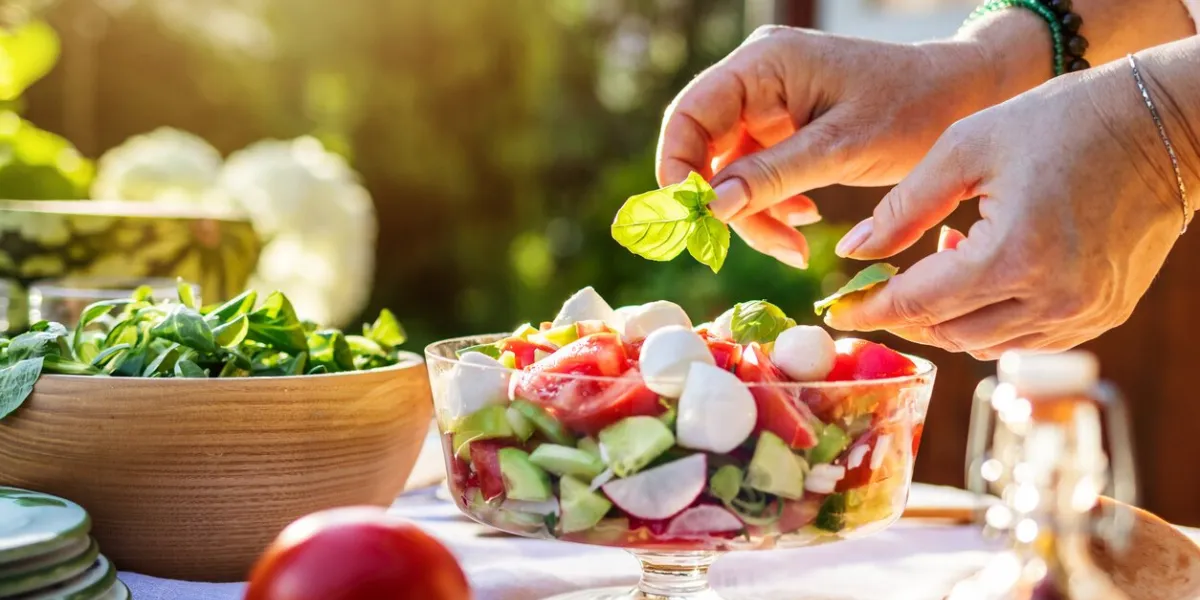 female hand finishing fresh vegetable salad with herb basil leaves preparing healthy food in garden outdoors
