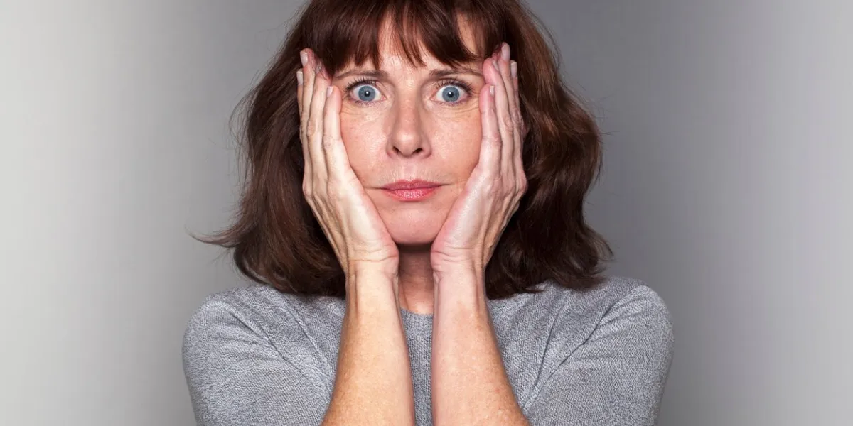 independent senior mature woman - portrait of anxious beautiful 50's woman under shock with both hands on face for fear and stress