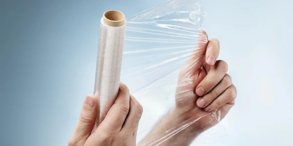 homme tenant un rouleau de film plastique, généralement utilisé pour sceller des aliments