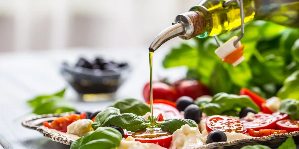 pouring olive oil on caprese salad healthy italian or mediterranean meal