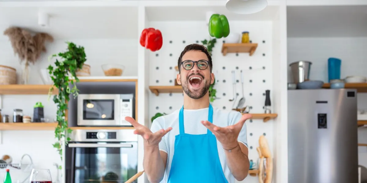 cheerful young man tossing vegetables in air at the kitchen