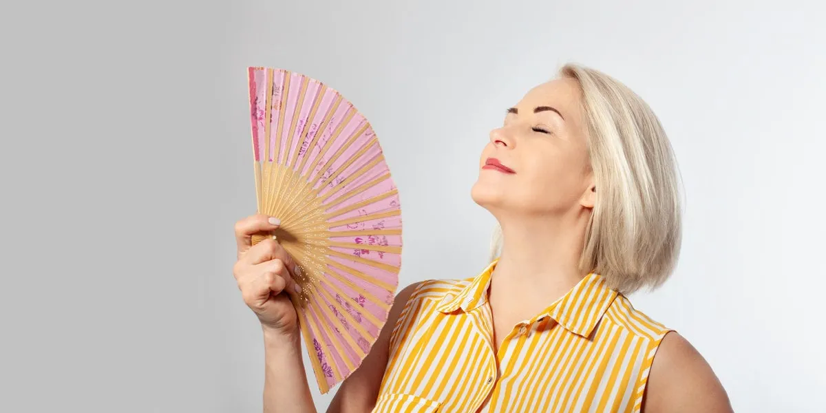 attractive middle aged woman relaxing with fan mature woman experiencing hot flush from menopause isolated on grey