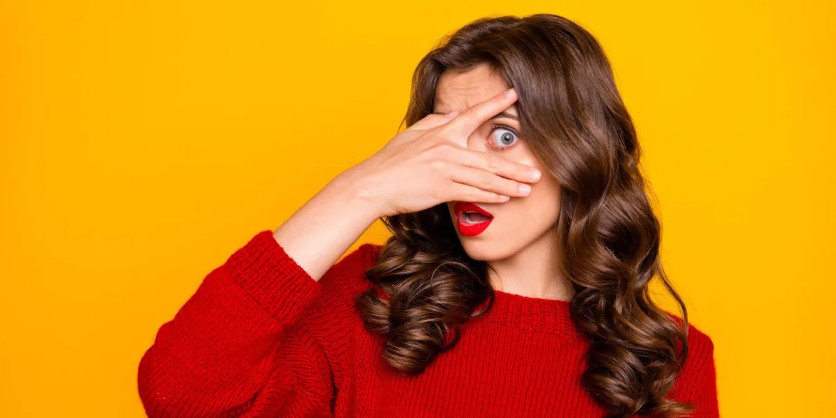 photo of curly wavy student trendy fearful astonished girlfriend looking out of her hand at something, terrible and unbelievable isolated over yellow vivid color background