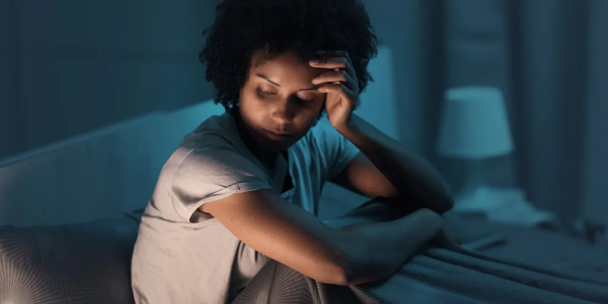 sleepless african american woman sitting in bed at night, she is stressed and unable to sleep