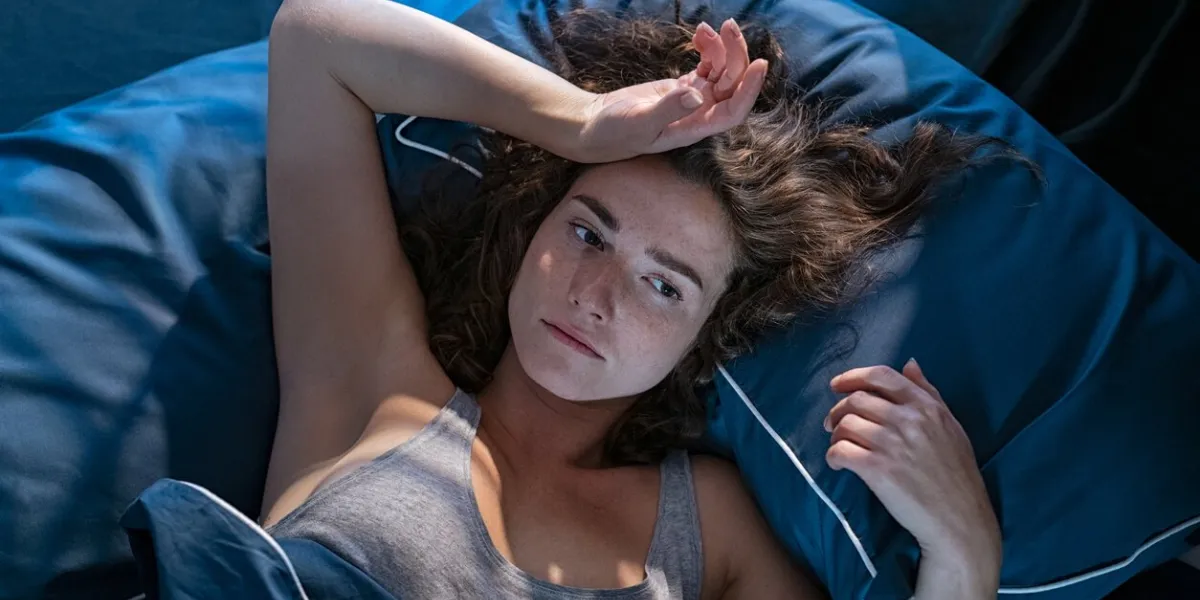 young stressed woman lying on bed late at night suffering from insomnia, sleep apnea or stress top view of depressed girl lying bed with dark pillow and blue blanket late at night high angle view of awake girl in the middle of the night